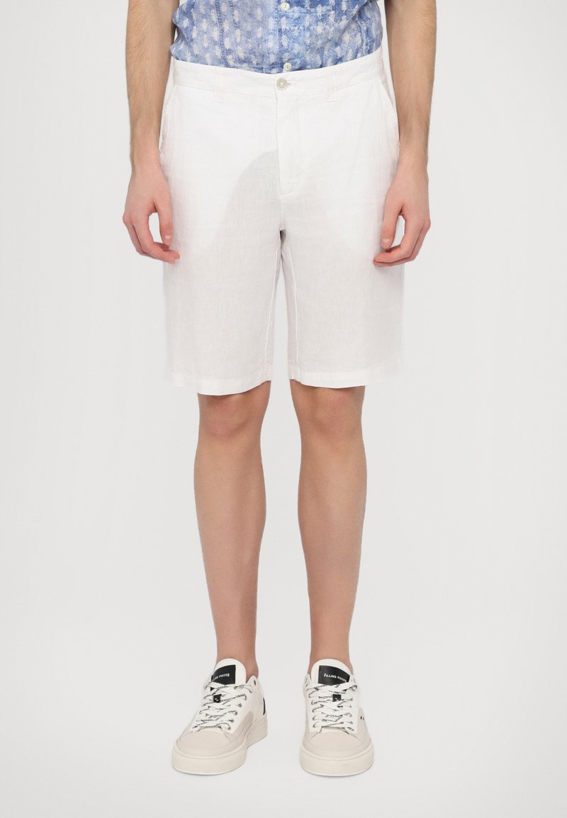 Shorts en lin blancs avec une texture lisse, dotés de deux poches avant et d'une fermeture à bouton, associés à des baskets beiges.