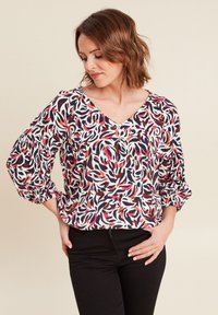 Blusa con stampa floreale, scollo a V, maniche puff e polsini elasticizzati. Motivi di foglie colorate in rosso, blu navy e crema su uno sfondo chiaro.