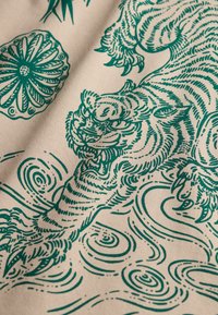 Illustrazione in inchiostro verde di una tigre ruggente con gli artigli estesi, circondata da motivi ondulati circolari, su uno sfondo di tessuto beige.