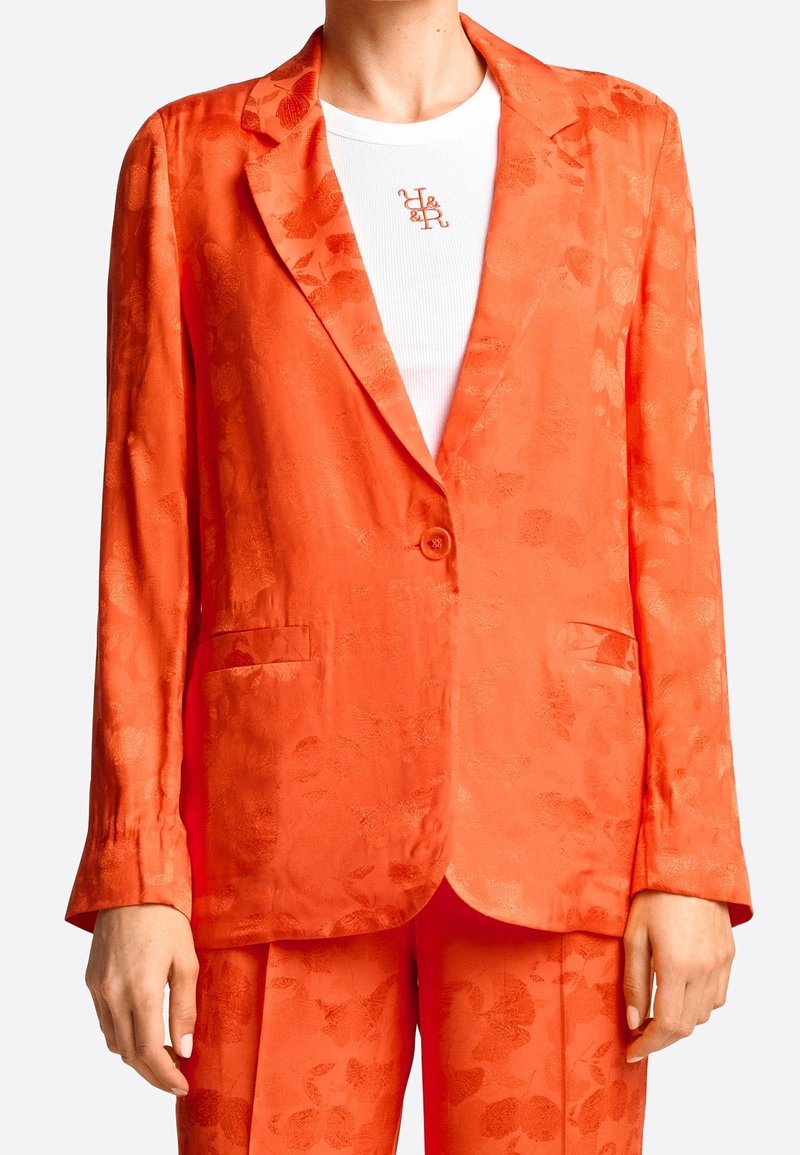 Blazer en satin orange avec un motif floral, fermeture à un bouton, revers crantés et deux poches avant. Assorti à une chemise blanche.
