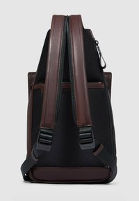 Zaino in tessuto nero con inserti in pelle marrone, doppie cinghie regolabili e due tasche con cerniera, caratterizzato da una superficie testurizzata.