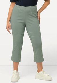 Pantalons cropped vert clair en tissu lisse, avec une taille haute et des plis subtils. Accompagnés de chaussures de sport blanches épaisses.