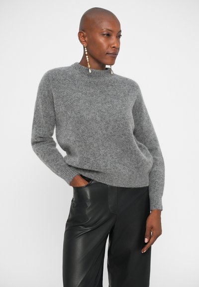 Maglione grigio in lana con colletto alto, maniche lunghe e polsini a coste, abbinato a pantaloni in pelle nera. Tessuto liscio, vestibilità comoda.