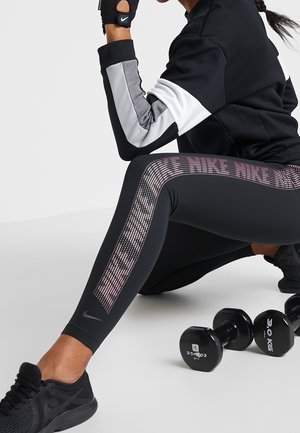 Czarne legginsy sportowe z różowym kropeczkowym wzorem po boku, w połączeniu z dopasowaną czarno-szaro długą koszulką oraz czarnymi sneakersami.