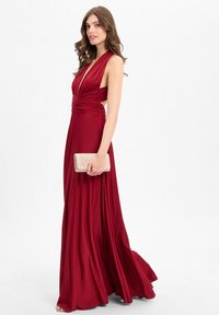 Rotes Abendkleid mit tiefem V-Ausschnitt, gerafftem Oberteil und fließendem Rock. Der glatte Stoff fällt elegant. Accessoire: glitzernde goldene Clutch.