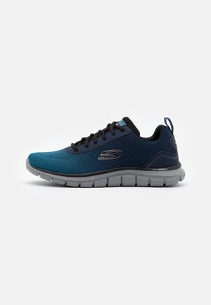 Zapatilla deportiva azul oscuro y negra con cordones, suela gris y logotipo de Skechers en el lateral, mostrada desde el lado exterior sobre fondo blanco.