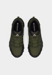 Ζεύγος πράσινων και μαύρων παπουτσιών πεζοπορίας Columbia με κορδόνια, υφασμένα πέλματα και λογότυπο στη γλώσσα και στην εσωτερική σόλα, στην όψη από πάνω.