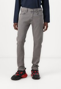 Grå denimjeans med rett snitt, fem-lommers design, kontraststing, og knappelukking. Brukt med svarte og røde sneakers.
