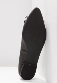 Chaussure plate noire avec une tige en cuir lisse, un bout pointu et une semelle en caoutchouc texturée. Accent métallique près du talon. Taille 37 indiquée sur la semelle.
