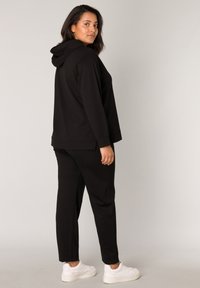 Zwarte hoodie en bijpassende broek, gemaakt van een zachte, rekbare stof. Bevat een capuchon, een ontspannen pasvorm en witte sneakers.