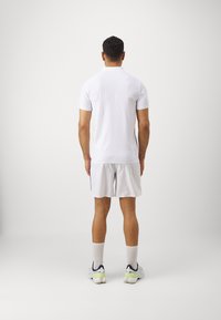 Herren Poloshirt in Weiß mit kurzen Ärmeln, kombiniert mit hellgrauen Shorts. Das Outfit hat ein einfaches Design und besteht aus leichtem Stoff.