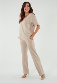 Beżowa bluzka z dekoltem w serek i krótkimi rękawami, zestawiona z luźnymi, beżowymi spodniami. Miękka tkanina o gładkiej fakturze i bocznymi kieszeniami.