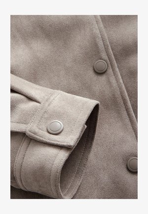 Helle graue Wildlederjacke mit glatter Textur, zwei großen Knöpfen und einem umgeschlagenen Bündchen mit einer Naht entlang der Kante.