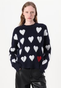Maglione fuzzy blu navy con motivi a cuore bianchi, caratterizzato da un singolo cuore rosso. Collo tondo, vestibilità morbida, con polsini e orlo a costine. Pantaloni in pelle nera.
