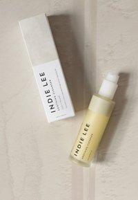 Indie Lee łagodzący środek czyszczący w przezroczystej butelce z białą pompką, zawierający żółty płyn. Towarzyszy mu biały prostokątny karton.