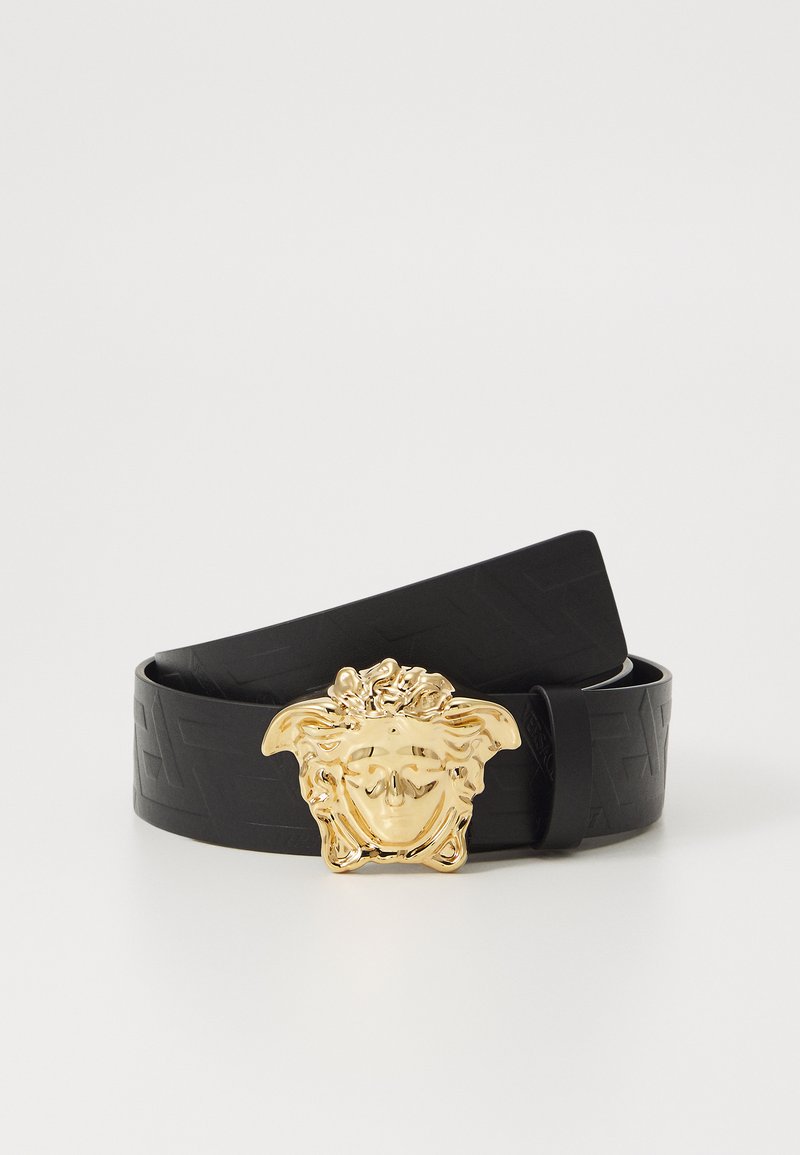 Cinturón de cuero negro con un patrón en relieve, que presenta una gran hebilla de metal dorado diseñada como un rostro estilizado con cabello detallado.