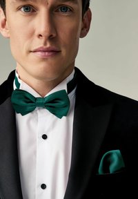 Tuxedo negru cu o textură satinat, cămașă albă și papion verde satinat. Include nasturi negri și un batiste asortată.