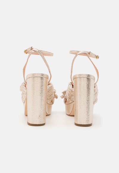Sandalias de tacón alto metálicas doradas con un tacón cuadrado grueso, tira en el tobillo y detalle de tela fruncida en la parte trasera. Acabado de textura suave.