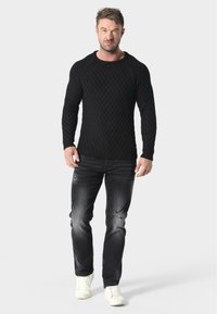 Czarny sweter dziany z teksturowanym wzorem, okrągłym dekoltem i dopasowanym krojem. Połączony z podartymi ciemnymi dżinsami i białymi sneakersami.