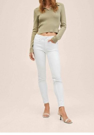 Pull cropped vert clair avec un col, associé à un jean blanc skinny. Présente une texture lisse et un design minimaliste, avec un éclat subtil.