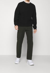 Black ribbed knit sweater, olive green pants, and white sneakers. The sweater has long sleeves and a crew neckline, with a textured finish.
