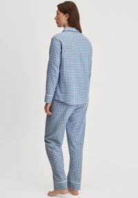 Set di pigiama a quadri blu e bianchi, composto da una camicia a maniche lunghe con bottoni e pantaloni abbinati con polsini, realizzati in un tessuto morbido.