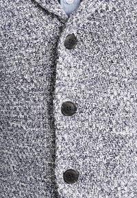 Szary i biały dzianinowy kardigan z teksturowanym wzorem, pięcioma guzikami i kołnierzem typu szalowego. Materiał wydaje się miękki i przytulny.