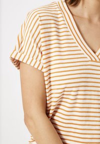 Camiseta de algodón con cuello en V, con rayas horizontales en naranja y blanco, mangas cortas enrolladas y un corte relajado.