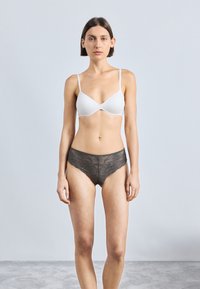 Soutien-gorge bianco a strappo sottile e finitura liscia, abbinato a perizoma in pizzo grigio scuro con motivi floreali e bordi ondulati.