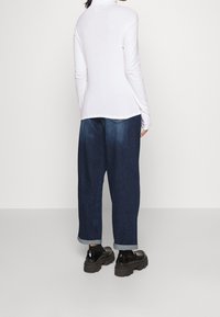 Vit långärmad topp med hög krage, matchad med lösa mörkblå jeans som är uppvikta vid fållarna, och kängor i kraftigt svart.