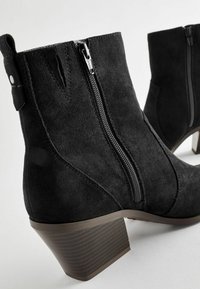 Černé semišové ankle boots se bočními zipy, texturovaným blokovým podpatkem a malým poutkem vzadu. Hladký povrch s čistými liniemi.