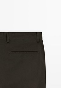 Donkergroene broek van gladde stof. Bevat riemlussen, een tailleband en een enkele achterzak met gestikt omtrek.