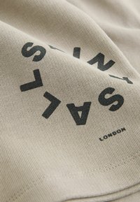 Bež tkanina z mehko teksturo ima debele črne črke in besedo "LONDON" blizu spodnjega roba, kar ustvarja grafični dizajn.