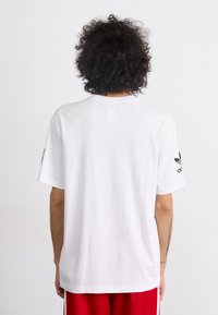 Hvit bomulls t-skjorte med rund hals og korte ermer. Har svart Adidas-logo på høyre erm. Enkel, uprydet bakdesign.