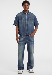Jeansjack met korte mouwen en twee borstzakken, gecombineerd met rechte denim jeans. Beide zijn in verschillende tinten blauw.