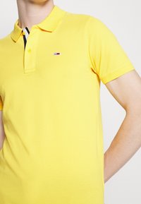 Polo shirt jaune en coton avec une patte de boutonnage à deux boutons, un petit logo sur la poitrine gauche et un design uni.