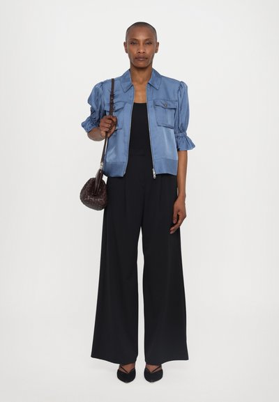 Zila īsā jakas ar pūkainām piedurknēm, priekšējiem kabatām un priekšējo rāvējslēdzēju, apvienota ar platām melnām biksēm un mazu brūnu somiņu.