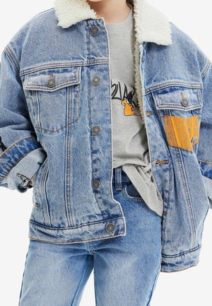 Jeansjack met een schapenvacht kraag, lichtblauwe kleur, versleten accenten en metalen knopen, gelaagd over een grijs shirt met een grafisch ontwerp.