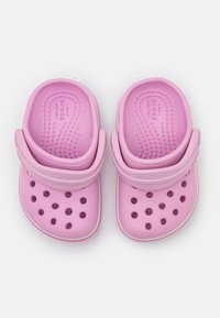 Růžové kroksy vyrobené z lehkého materiálu, s texturovaným povrchem, kulatými ventilačními otvory a měkkým popruhem pro bezpečné uchycení.