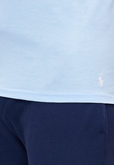 Light blue cotton t-shirt with a rounded hem and white embroidered logo; paired with navy textured fabric shorts.