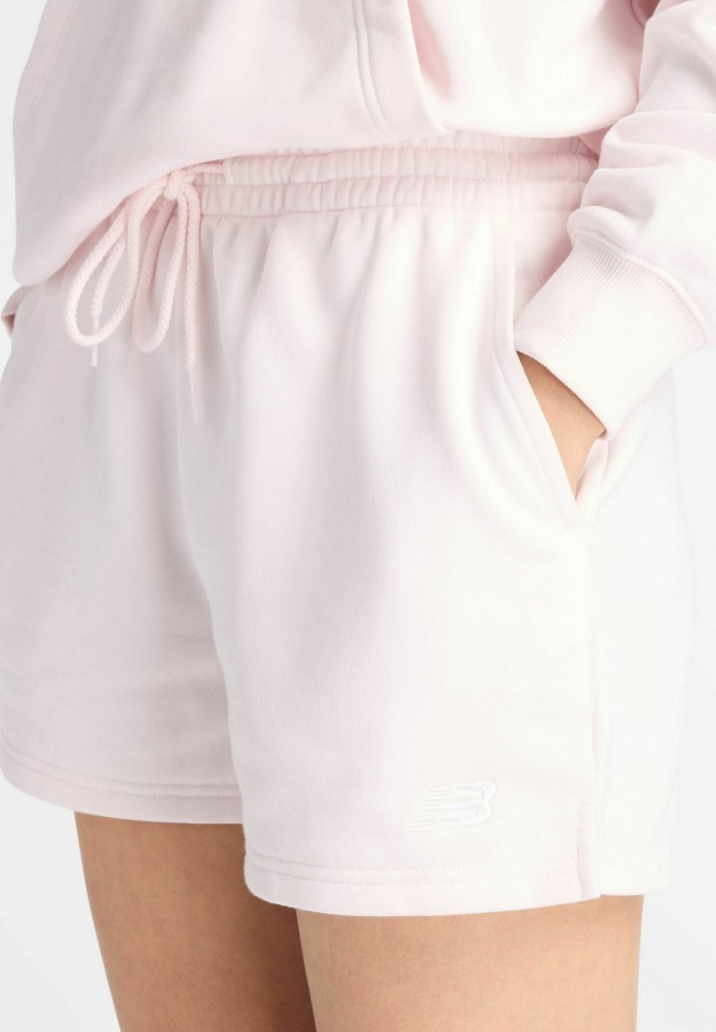 Lichtroze short met trekkoord en zijzakken, gedragen door een persoon met één hand in de zak, met een zachte stof en een elastische tailleband.