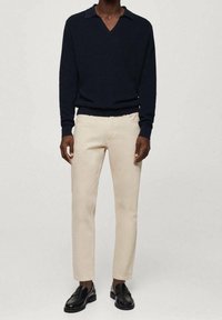 Suéter de punto azul marino con escote en V y cuello, combinado con pantalones beige de corte slim y mocasines de cuero negro. Diseño simple y elegante.