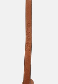 Pasek do torby z skóry Calvina Kleina w bogatym brązowym kolorze z ziarnistą fakturą, z wytłoczonym logo i kontrastującym przeszyciem na krawędziach.