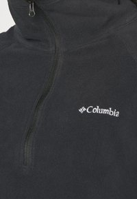 Schwarzer Fleece-Pullover mit hohem Kragen, halbem Reißverschluss und weißem Columbia-Logo auf der linken Brustseite. Weiche Textur.