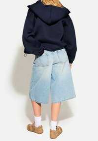 Námořnická mikina s kapucí, světle modré denim bermudy, béžové tenisky, bílé ponožky, volný střih, viditelné zadní kapsy a texturované materiály.