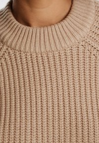 Jersey beige de punto con textura acanalada, escote redondo y detalles sutiles en las costuras. Material suave, grueso y elástico.