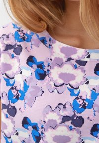 Top con motivo floreale caratterizzato da una base lavanda con fiori blu e viola scuro. Tessuto testurizzato, scollatura rotonda, maniche corte.