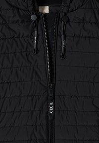 Schwarze gesteppte Jacke mit zentralem Reißverschluss und verstellbaren Kordeln, jeweils mit dem weißen Schriftzug "CECIL" versehen.