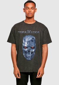 Crna oversized majica od pamuka s velikim plavim i crvenim grafikonom robotske lubanje te natpisom "THE TERMINATOR" iznad.