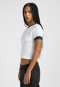 Hvid cropped t-shirt med ribbet tekstur, korte ærmer og marineblå halsudskæring. Sammen med mørke denim jeans.